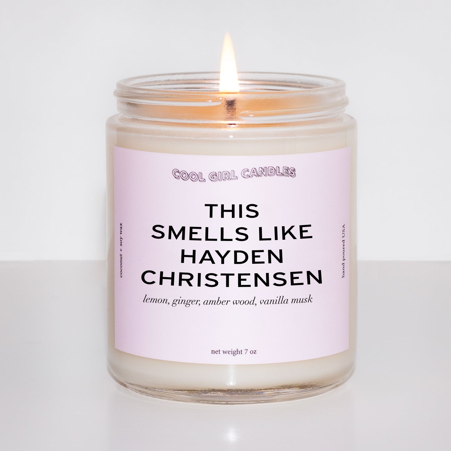 Candle in a glass jar with a pink label on a white background. The pink label says This Smells Like Hayden Christensen and is made by Cool Girl Candles