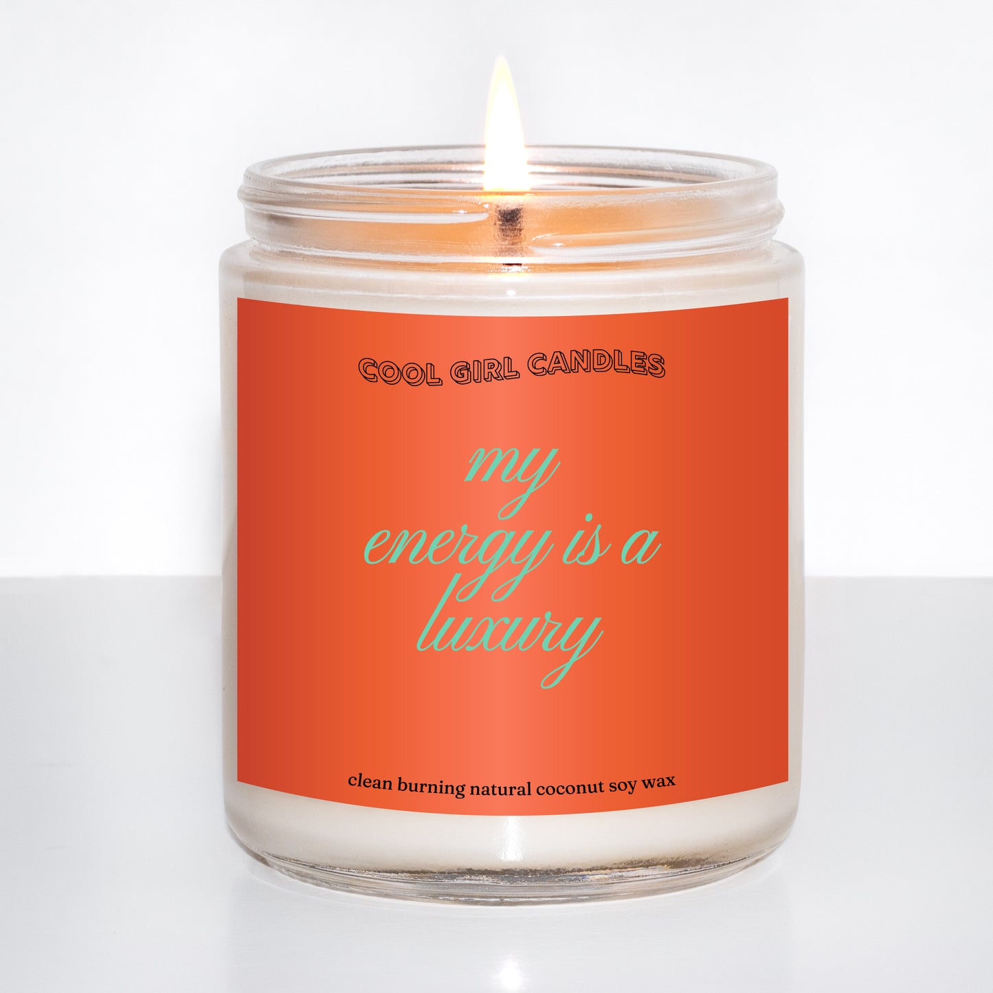 Candle in a glass jar with an orange label on a white background that says "my energy is a luxury" which is a quote from Taylor swift and makes for the perfect Taylor swift fan gift