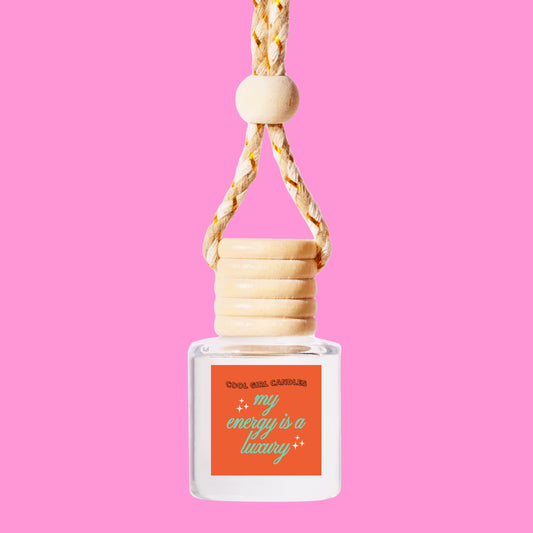 a hanging scented car freshener glass bottle with a label that says "my energy is a luxury" - a quote from Taylor swift that makes for a great swiftie gift, made by cool girl candles